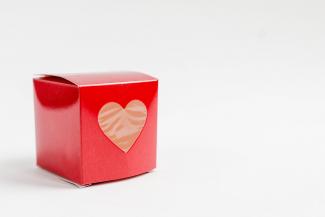 Beyaz zemin üzerinde kırmızı kartondan bir hediye kutusu ve kutunun üzerinde kalp şeklinde bir pencere var.