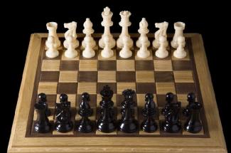 Ahşap bir satranç tahtasında karşılıklı iki grup taşlar dizilmiş, oyuna hazır halde.