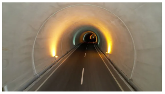 Görselde boş bir karayolu tünelinin içi fotoğraflanmış. Tünelin tavanından yan duvarlara inen ışıklar, yarım çember şeklinde görünüyor ve tünel boyunca birbirini izliyor.