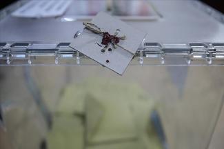 Tam ekran olarak flu görüntülenen oy sandığının içerisinde zarflar bulunuyor. Görselin tam ortasında yer alan sandık kapağındaki mühür yakın çekimde net olarak görüntülenmiş.