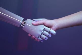 Mavi bir arka plan. Sol taraftan uzanmış bir robot kol ve sağ taraftan uzanmış bir erkek kolu el sıkışıyor.