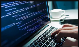 Siyah çerçevenin içerisindeki fotoğrafta, dizüstü bilgisayarın ekranında program kodları ve klavyesinde bir erkek eli görüntüleniyor. Dizüstü bilgisayarın bulunduğu masanın sağ tarafında ise bir fincan ve cep telefonu yer alıyor.