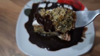 Ahşap olduğu anlaşılan bir masanın üstünde beyaz bir tabak. Fotograf tabağın içindeki tatlıya odaklanmış, diğer kısımlar bulanıklaştırılmış. Yakın planda bir çatal ve üzerine çikolata soslu, haşhaşlı kekle yapılmış tatlı parçası ve tabağın içerisinde bol çikolata sosunun içerisinde bir dilim tatlı görüntüleniyor.