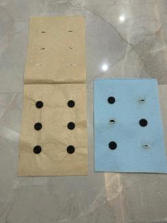 Üstten çekilmiş fotoğrafta mermer zeminin üzerinde iki farklı renkte keçe var. Sol tarafta duran keçe  kahverengi ve dikey olarak katlanmış. Üst yarısında üç sıra halinde 6 küçük kesik var.  Her sırada 2 kesik mevcut. Alt yarısında ise yine dikey olarak üç sıra halinde düzenlenmiş altı adet koyu kahverengi düğme bulunuyor ve yine her sırada iki düğme var. Sağ tarafta ise açık mavi renkte bir keçe görülüyor.  Bu kumaş parçasında da düğmeler ve kesikler var.